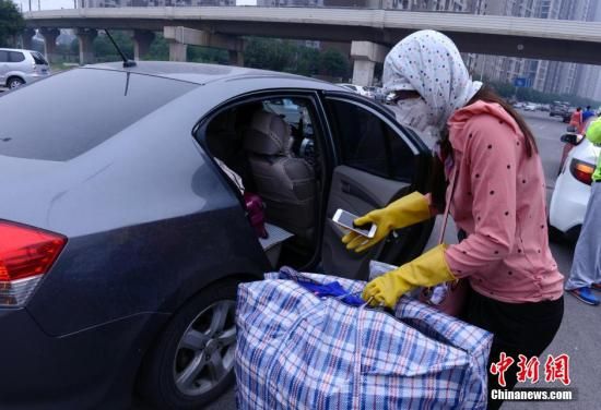8月18日下午，天津港爆炸现场附近的小区居民搬运生活用品离开。图为一位姑娘在简单防护后把生活品塞进轿车里。中新社发 贾国荣 摄
